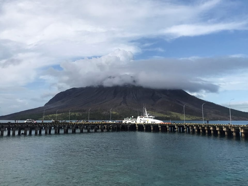 Schiff am Pier mit Berg im Hintergrund, teilweise von Wolken bedeckt.