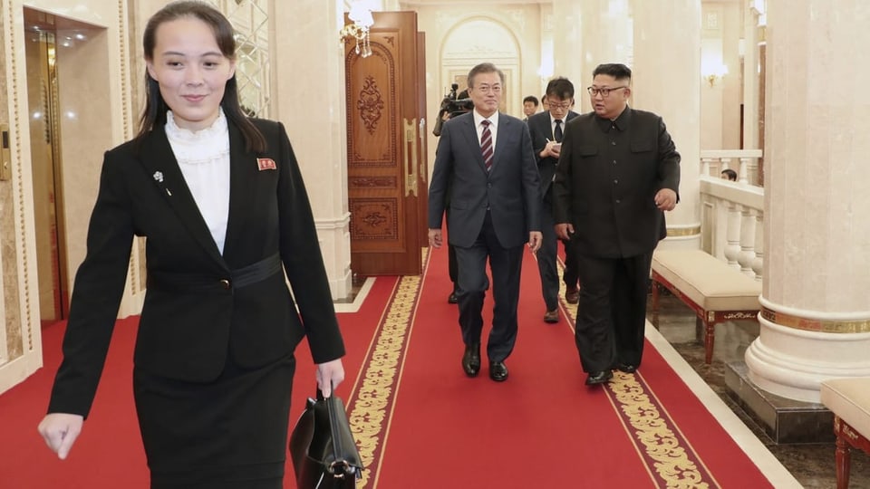 Kim Yo-jong vorne mit Aktentasche, Kim Jong-un und Moon-Jae-in weiter hinten auf rotem Teppich.