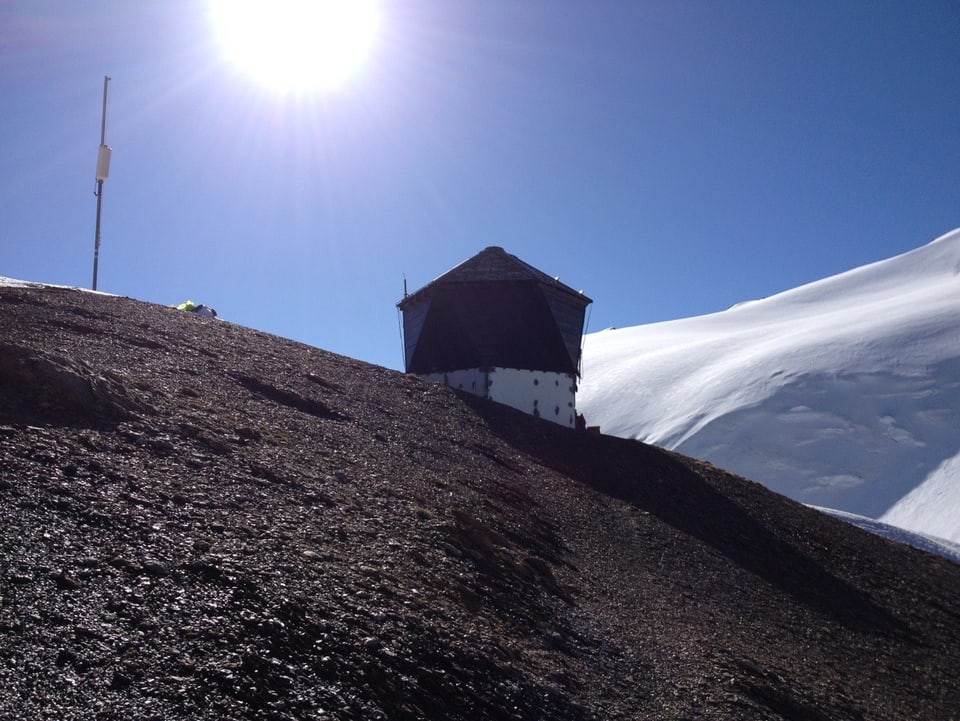 SAC-Hütte mit Sonne und Schneeberge im Hintergrund.