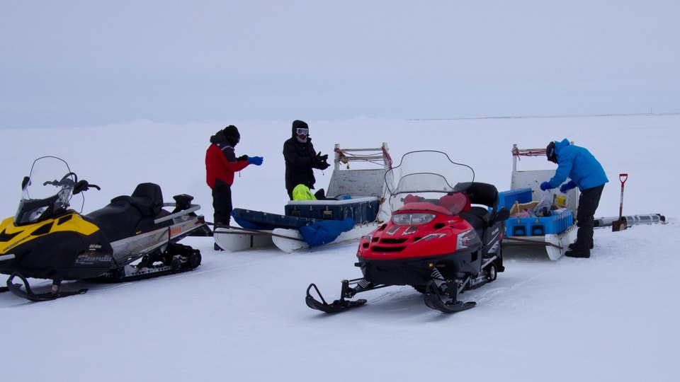 Die Forscher mit Schneemobilen und Material auf dem Eis.
