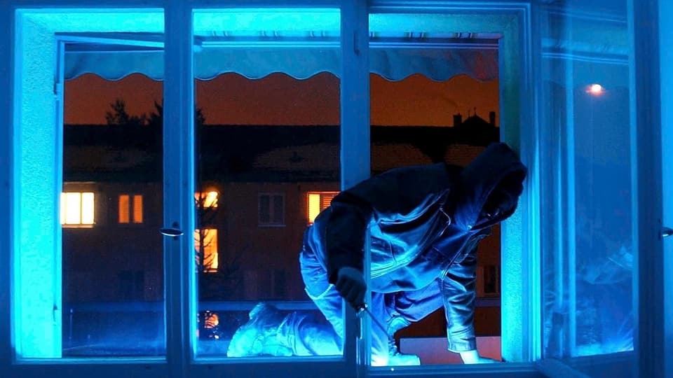 Einbrecher steigt bei Dunkelheit über ein Fenster in eine Wohnung ein