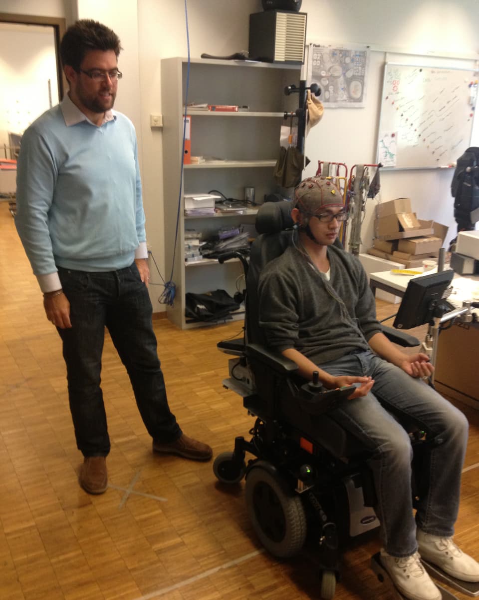 Alex Zhang versucht mit dem Rollstuhl zu fahren. Der Forscher steht dahinter.