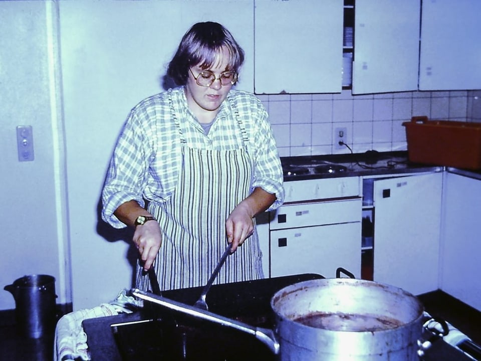 Frau kocht in einer Küche mit weisser Einrichtung.