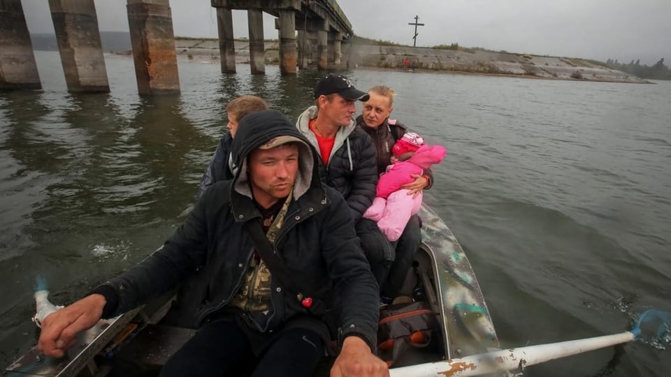 Menschen in einem Ruderboot, dahinter zerstörte Brücke.