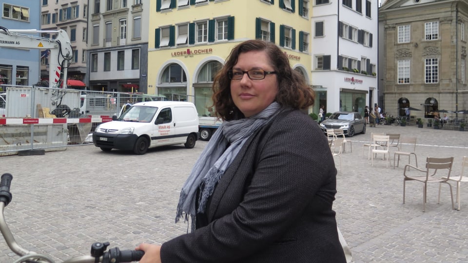 Eine Frau im Halbporträt steht mit ihrem Velo auf dem Münsterhof