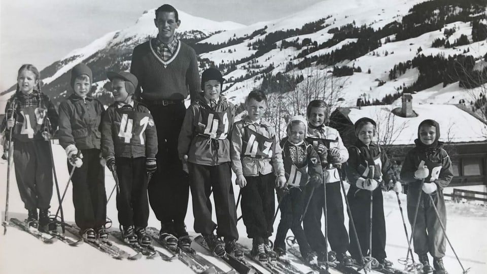 Eine Gruppe von Mädchen und Buben mit einem Lehrer auf Skiern.