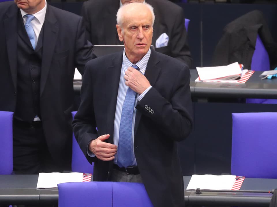 Albrecht Glaser stehend im Bundestag mit einer Hand am Krawattenknoten.