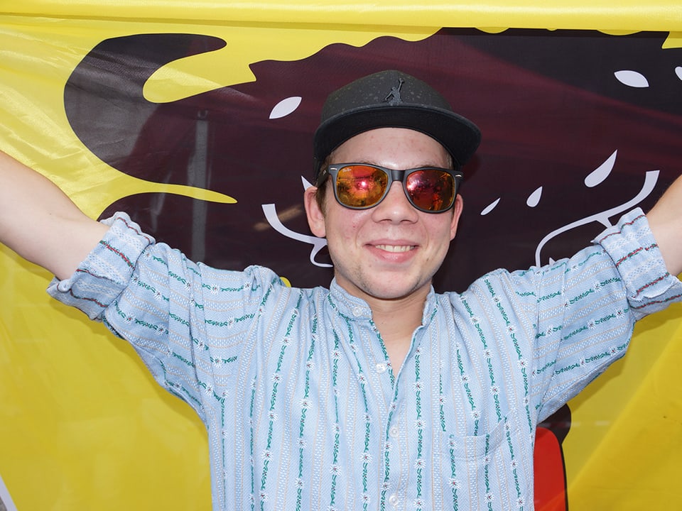 Ein Mann mit Mütze, Sonnenbrille und Sennenhemd vor einer Kantonsflagge.