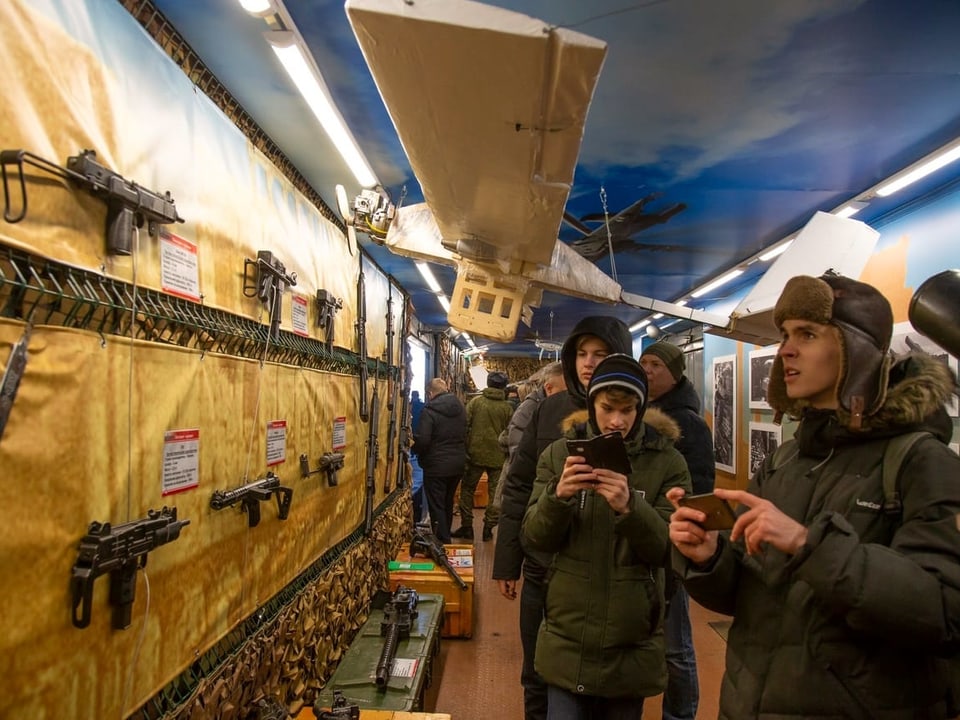 Besucher schauen im Zug auf präsentierte Gewehre.