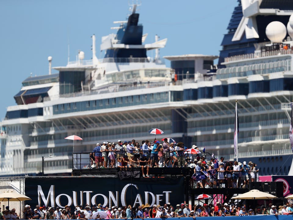 Ein Kreuzfahrtschiff und Zuschauer auf einer Tribüne verfolgen die Rennen.