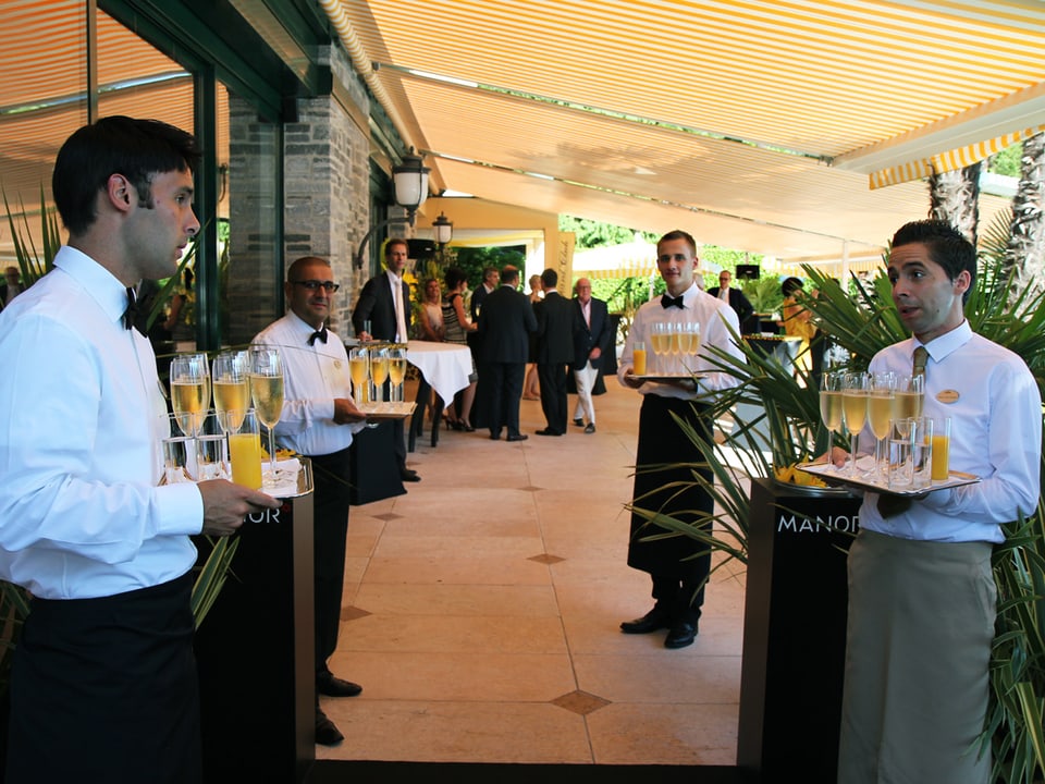 Kellner halten auf einer Terrasse Champagner auf Tableaus bereit.