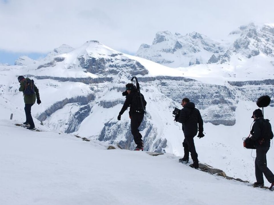 4 Männer stapfen durch die schneebedeckte Berglandschaft