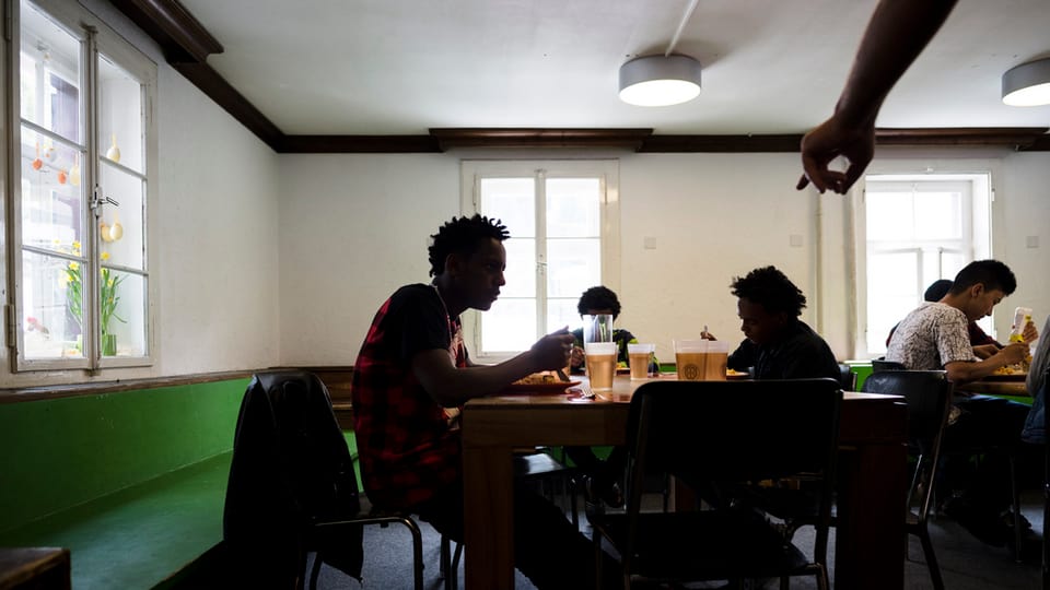 Junge Asylsuchende sitzen an Tischen 