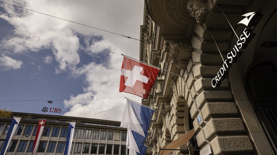 Die UBS und die CS stehen sich gegenüber. Dazwischen sind die Schweizerflagge und Zürichflagge zu sehen.