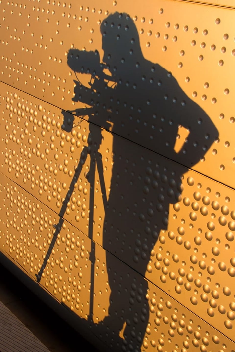 Ein Fotograf wirft seinen Schatten auf eine goldene Wand.