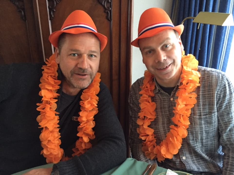 Zwei Männer mit orangefarbenen Fasnachtshüten und orangen Girlanden um den Hals.