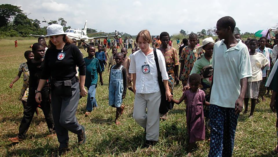 IKRK-Mitarbeiter laufen gemeinsam mit afrikanischen Menschen über einen Wald-Landeplatz.