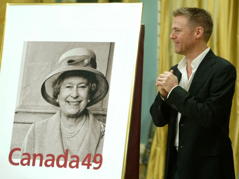 Sänger Bryan Adams steht neben dem Foto von Königin Elisabeth, welches als Briefmarke verwendet wird.