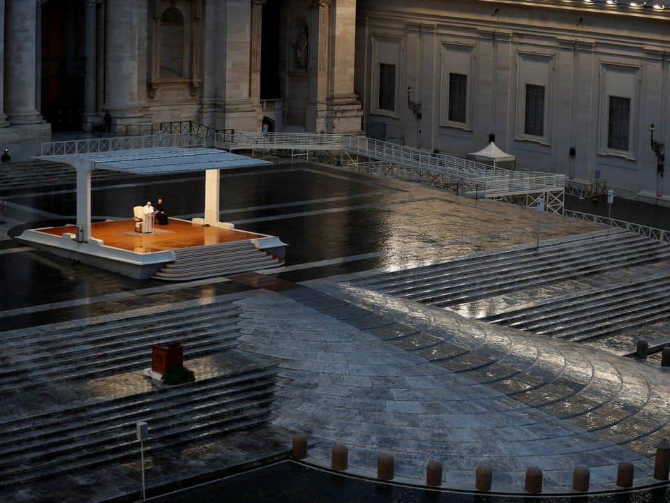 Papst Franziskus sitzt auf einem beleuchteten Podium vor einem menschenleeren Petersplatz in Rom