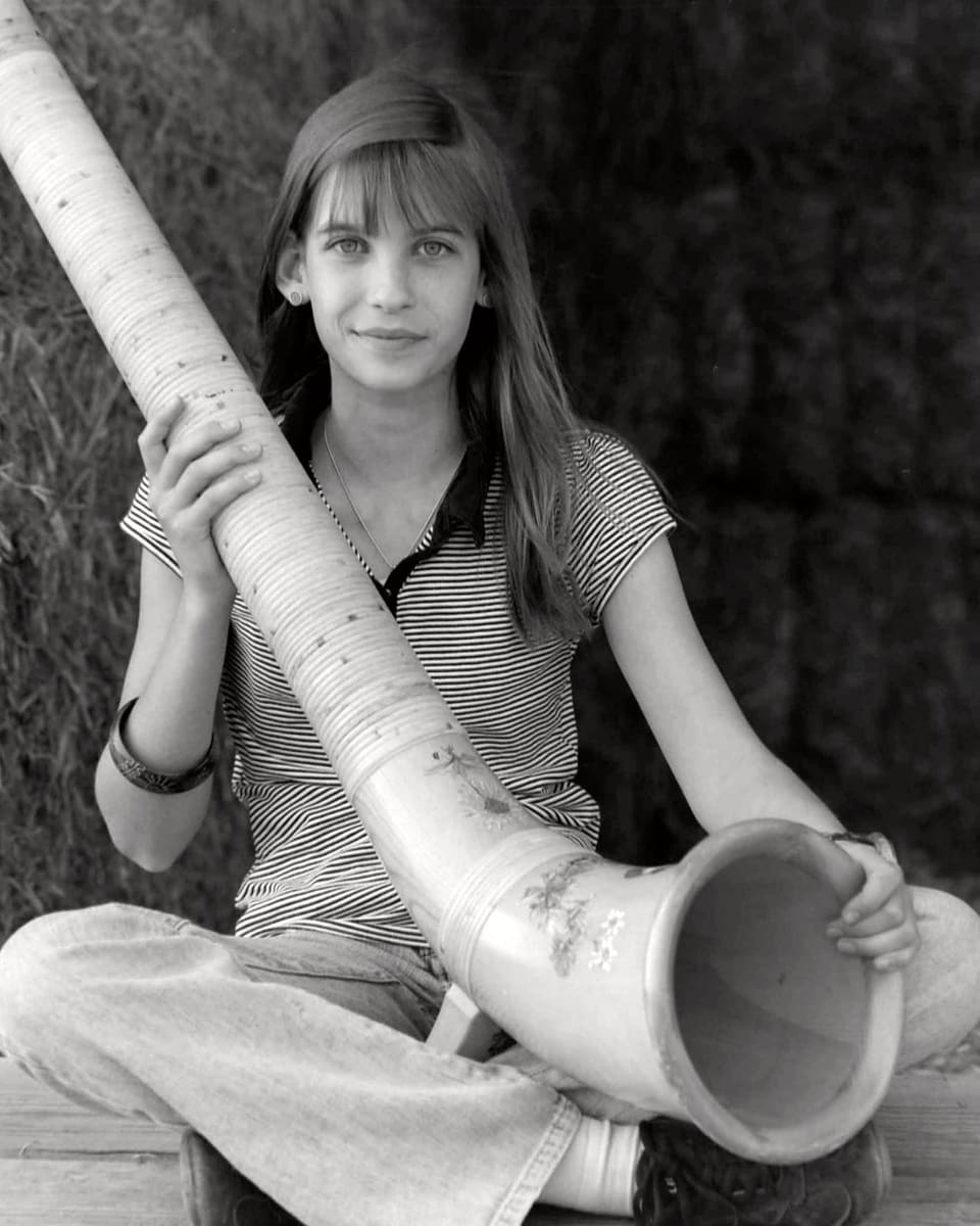 Schwarz-Weiss-Fotografie von einem Mädchen mit einem Alphorn.
