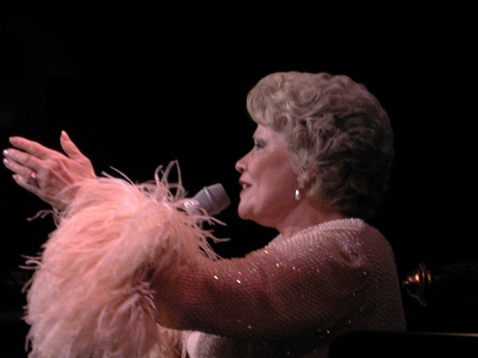 Patti live in rosa, glitzerndem Kostüm und Federboa.