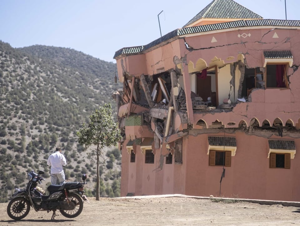 Ein Mann steht mit einem Motorrad neben einem zerstörten Gebäude in Marrakesch.