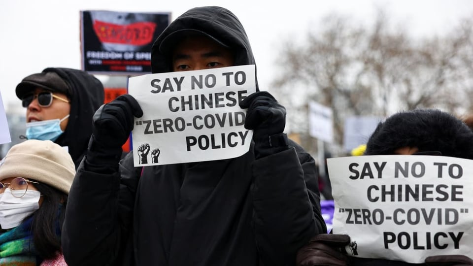 Menschen in China protestieren. Zwei Menschen halten ein Papier mit den Worten «Say no to chinese zero-covid policy».