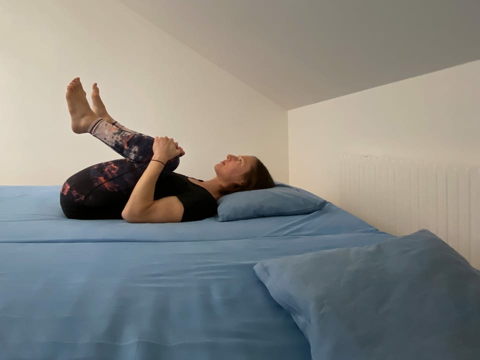 Frau liegt auf Bett und zieht Knie zur Brust.