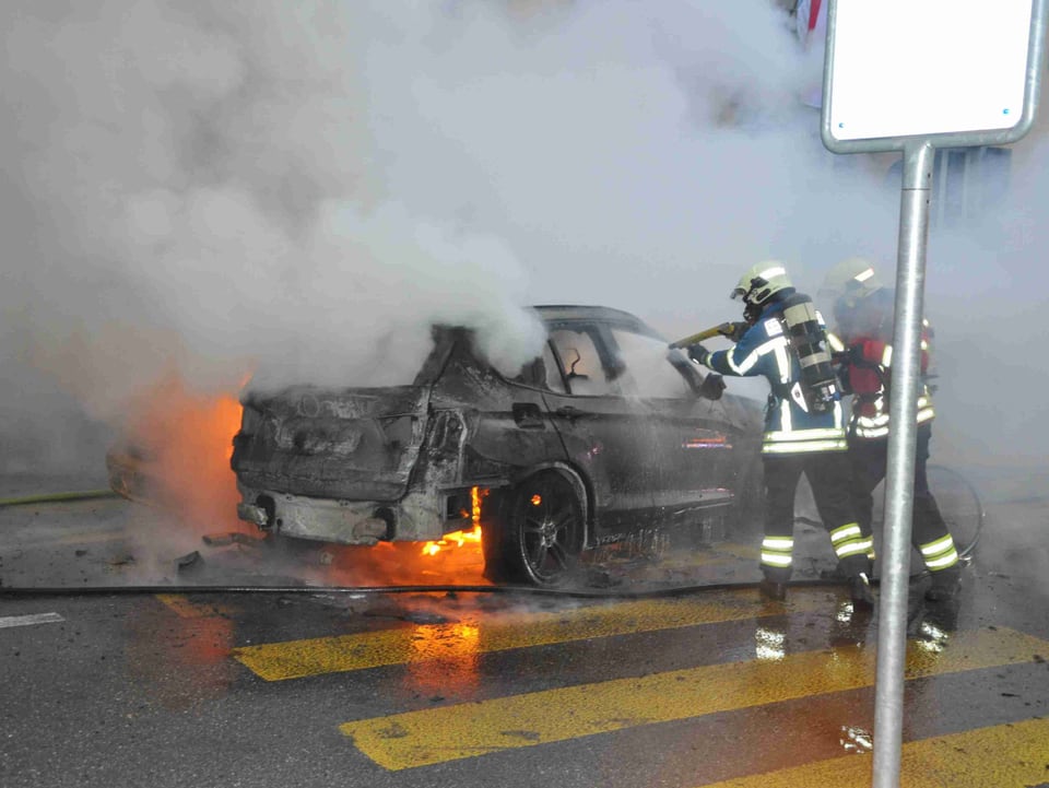 Zwei Feuerwehrmänner löschen brennendes Auto.