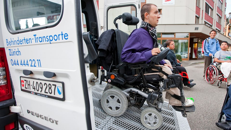 Invalider fährt auf Rampe aus einem Transporterbus heraus.