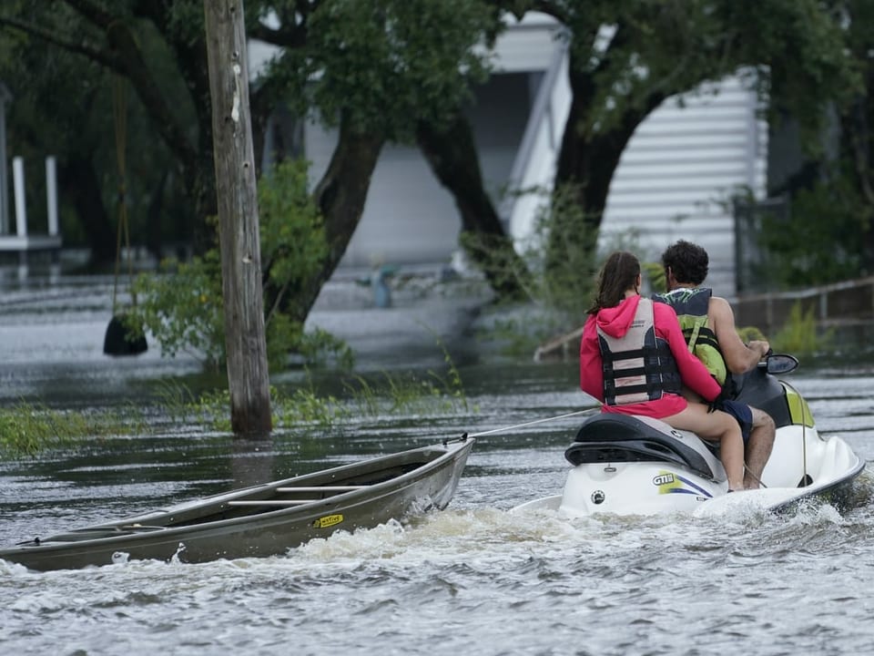 Anwohner auf einem Jetski schleppen ein Kanu zu einem überfluteten Haus.