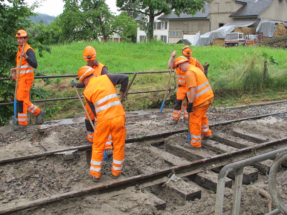 Arbeiter in orangen Kleidern auf einem Bahngeleise.