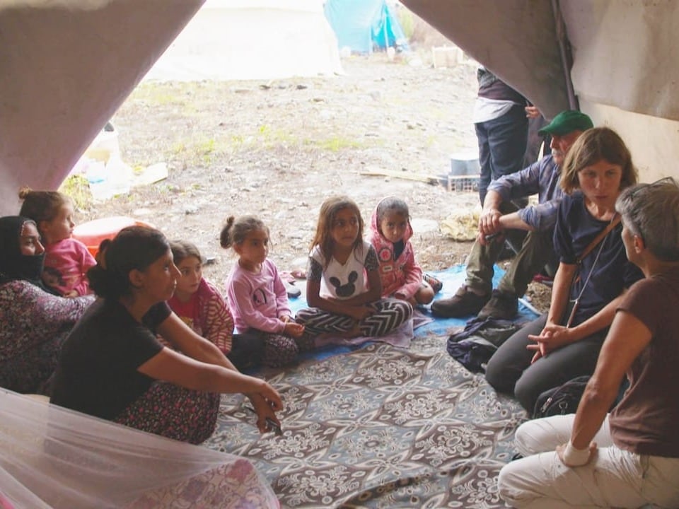 Mehrere Kinder sitzen in einem kleinen Zelt, zusammen mit Reporterin Marianne Kägi.