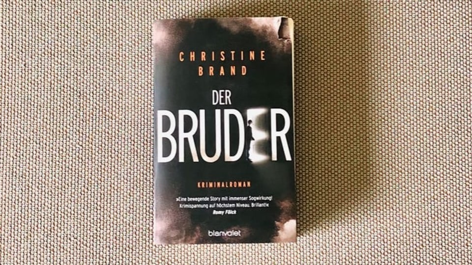 Krimi Nummer 3 «Der Bruder» von Christine Brand liegt auf einem beigen Sofastoff