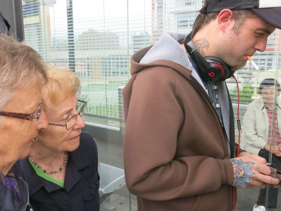 Zwei Seniorinnen schauen einem jungen Mann beim Ticketkauf zu.