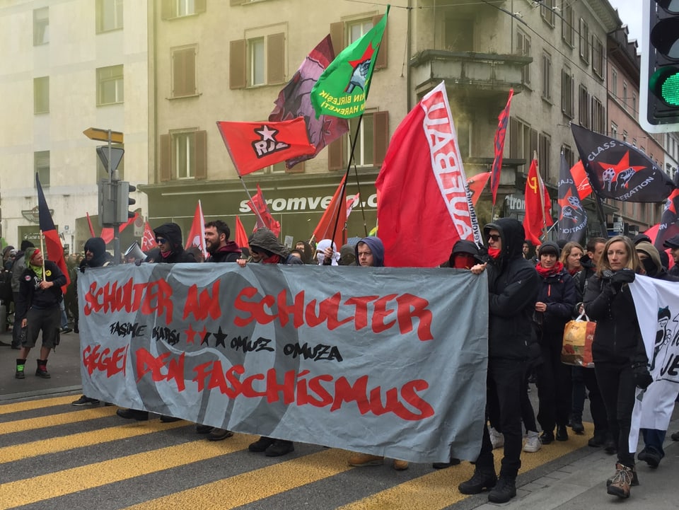 Schwerz gekleidete junge Leute rufen mit einem Transparent zum Schulterschluss gegen den Faschismus auf