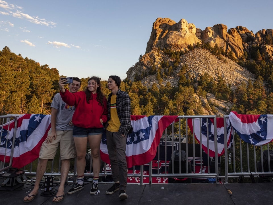 Drei Teenager machen ein Selfie vor einem Felsen mit Präsidentengesichtern