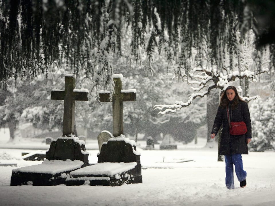 Eine Frau läuft durch einen verschneiten Friedhof.