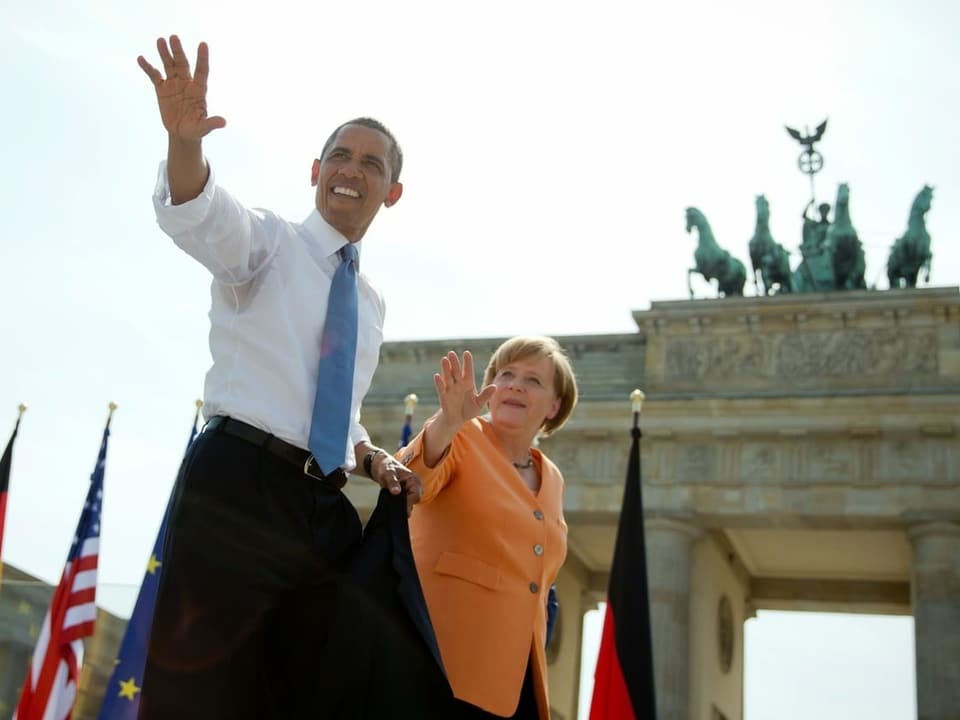 Obama hält Merkel bei der Hand, sie stehen vor dem Brandenburger Tor.