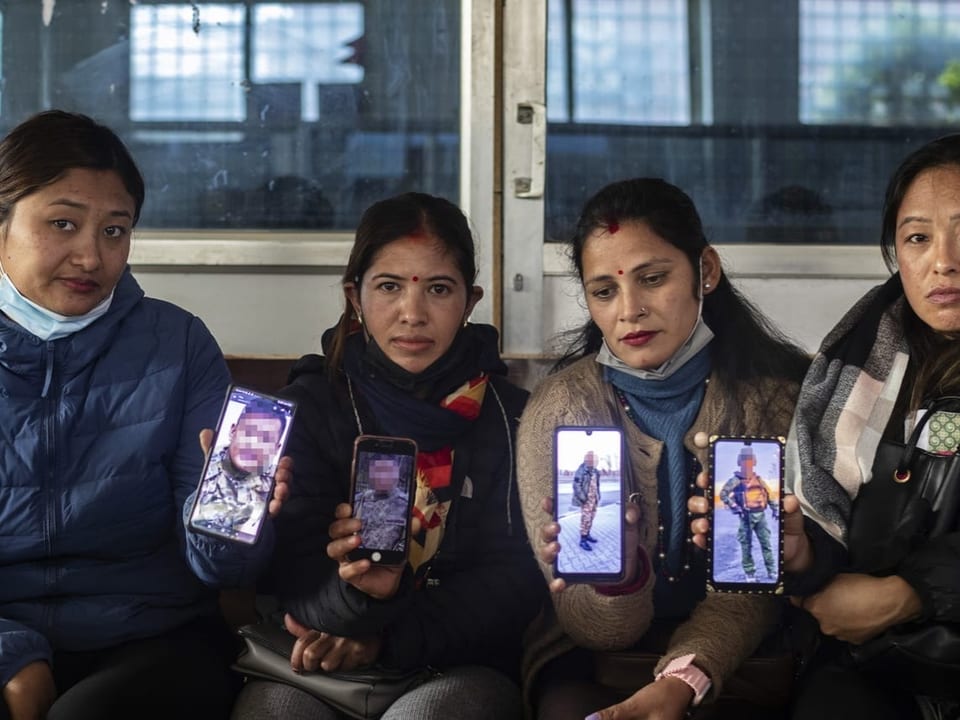 Vier Frauen sitzen nebeneinander und halten ihre Smartphones nach oben. Darauf sind Soldaten zu sehen.