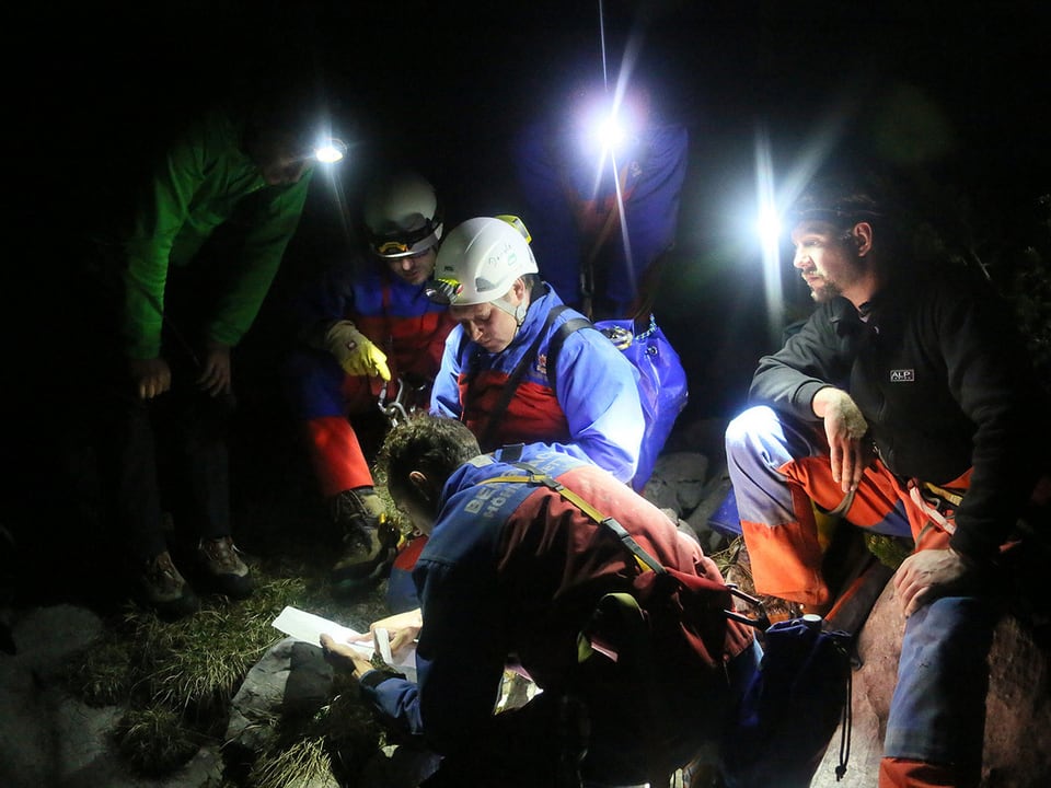 Einsatzkräfte der Bergwacht sitzen gemeinsam im Dunkeln mit Stirnlampen vor einer Karte, sie beraten sich. 