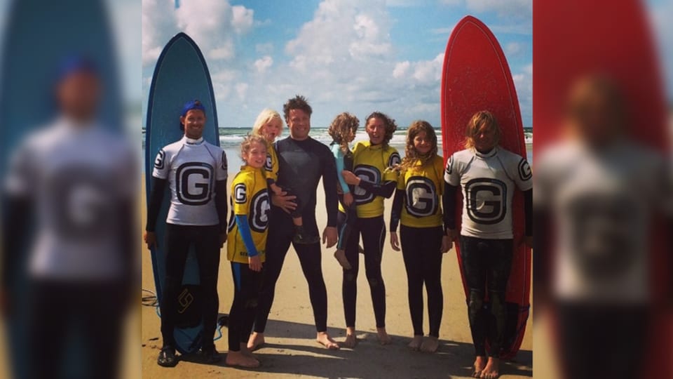 Familie Oliver zu viert am Strand, daneben zwei weitere Surfer