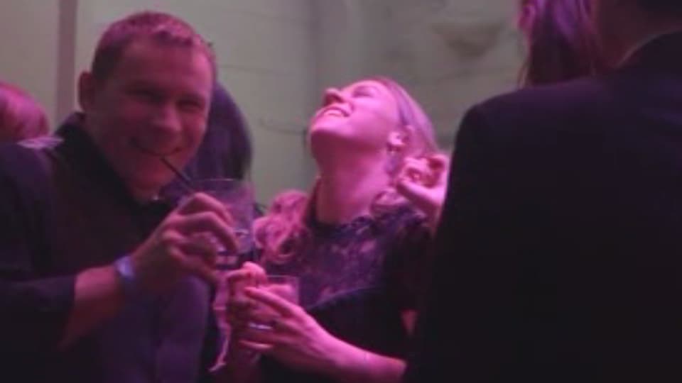 Ein Mann und eine Frau stehen auf einer Party nebeneinander, beide mit Drinks in der Hand.