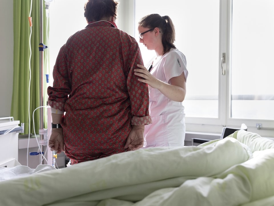 Eine Pflegefachfrau stütz eine Person neben einem Spitalbett.