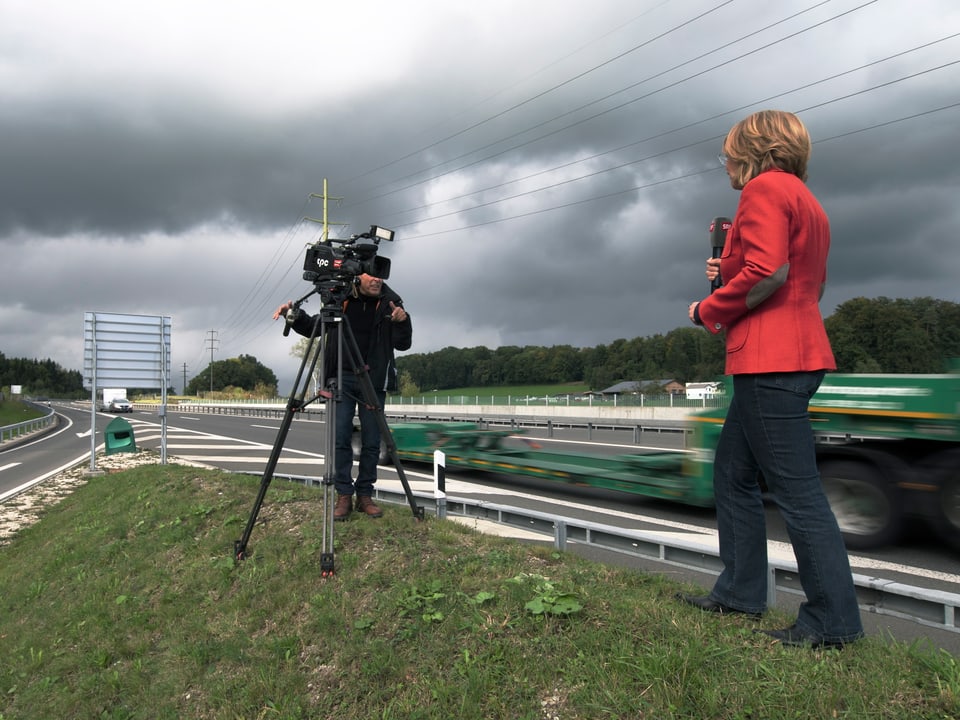 Sonja Hasler steht zusammen mit einem Kameramann neben der Autobahn.