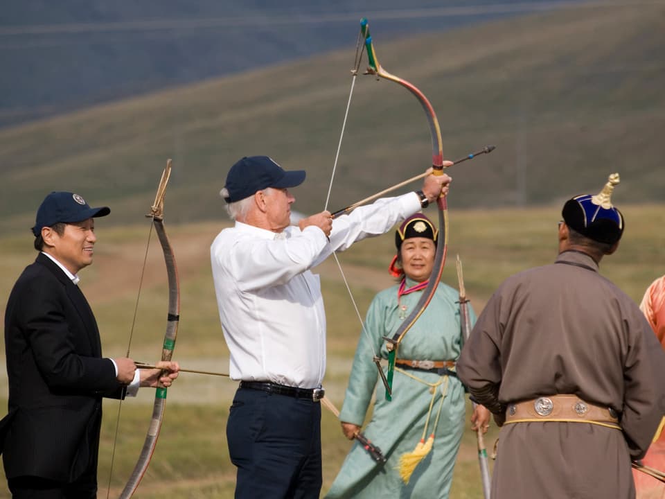 Joe Biden spannt einen Bogen und der Mongolische Premierminister schaut ihm zu.