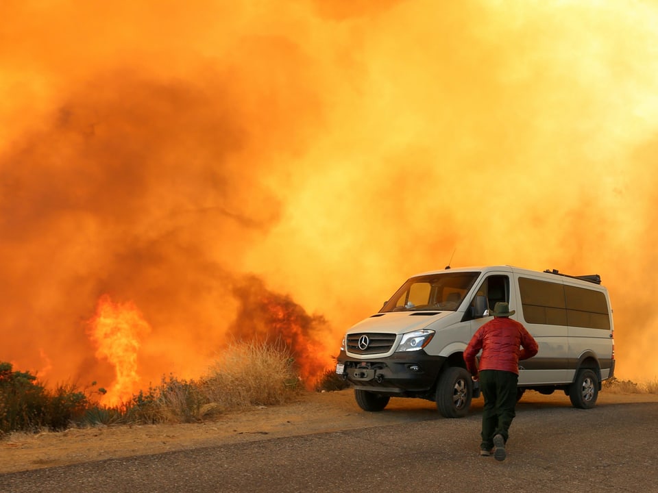 Mann rennt zu seinem Wagen vor einer Feuerwand