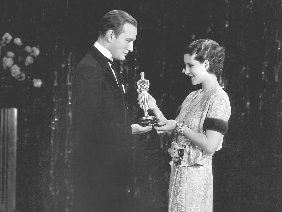 Eine Frau überreicht einem Mann einen Oscar (Schwarz-Weiss-Bild)