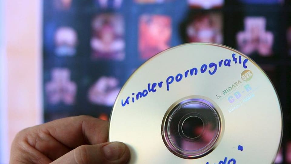 Ein Mann hält eine CD mit der Aufschrift Kinderpornografie vor einem Bildschirm.