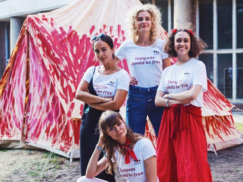 Vier junge Frauen posieren vor einem rot angemalten Zelt.